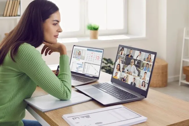 Sitzende Frau mit Laptop und Tablet am Tisch vor sich