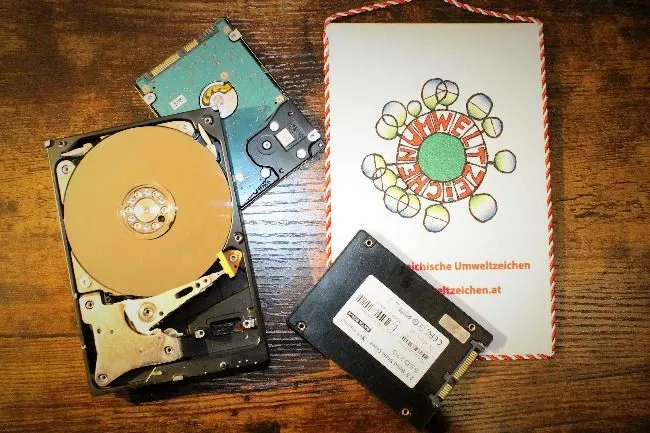 Alte Festplatten und eine neue SSD, liegen gemeinsam am Tisch mit dem Umweltzeichen.
